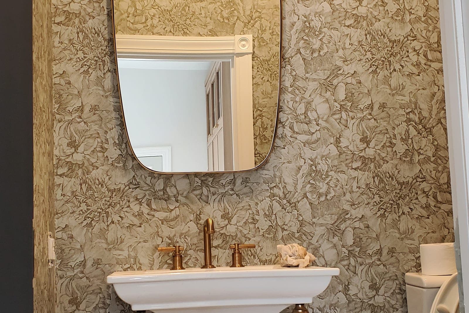 Powder room with metallic floral wallpaper, a pedestal sink and an arched mirror