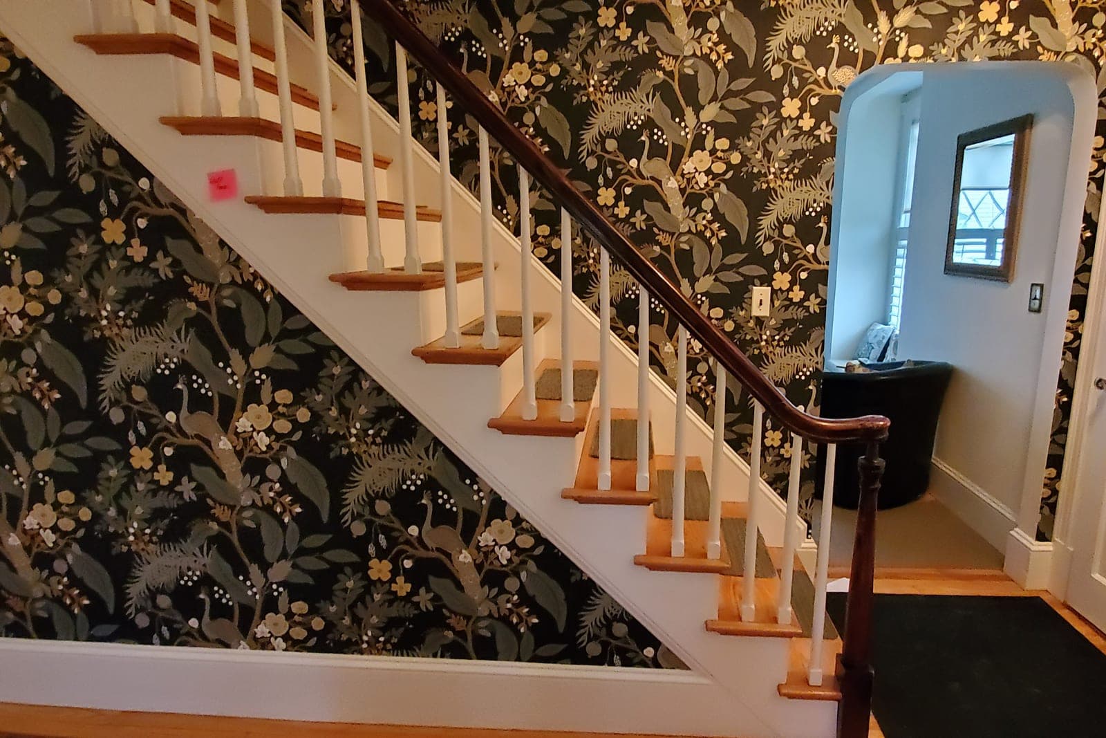 Stairwell and entry hall papered in a dark botanical print with white balusters