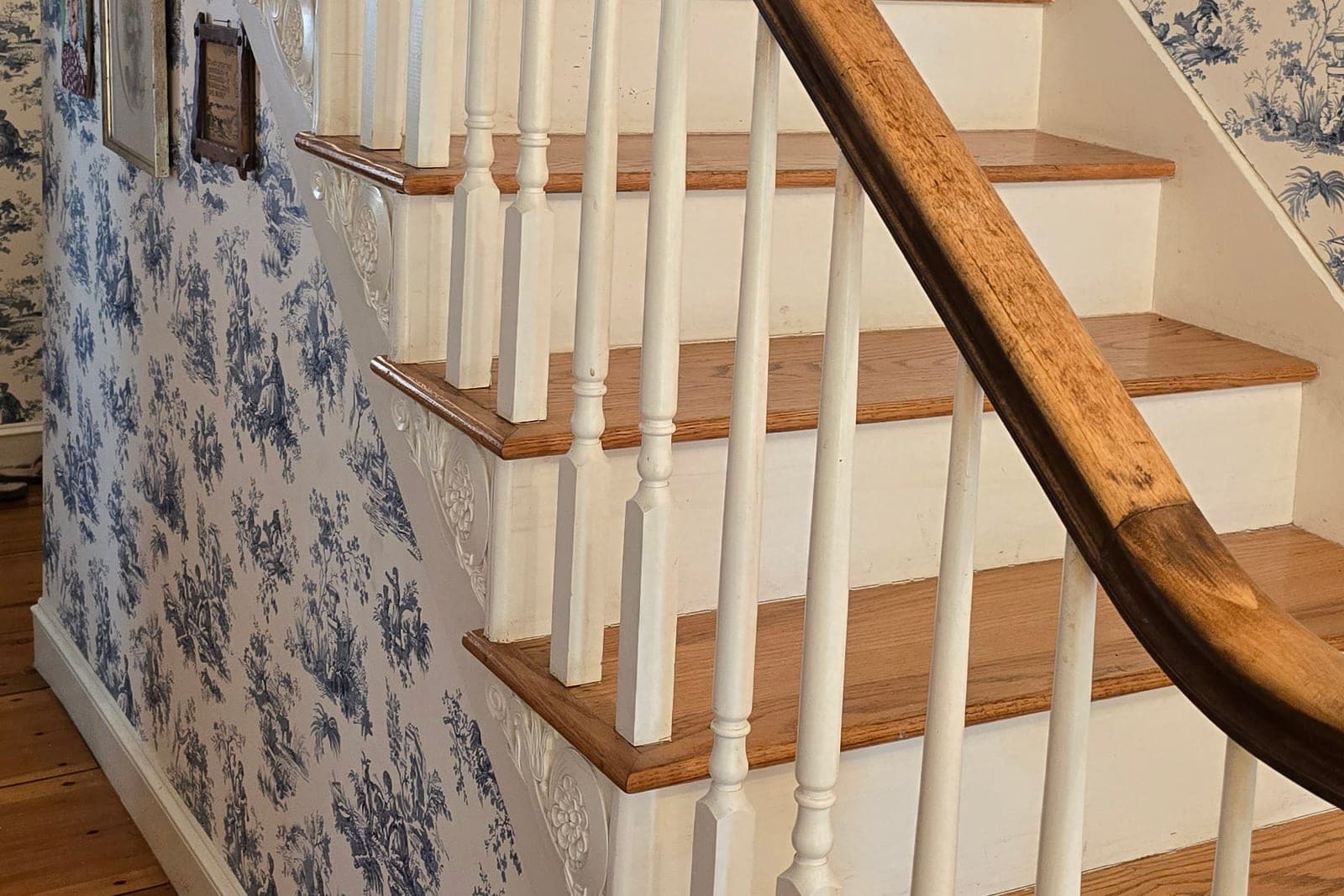 Staircase with blue-and-white toile wallpaper and a wood handrail
